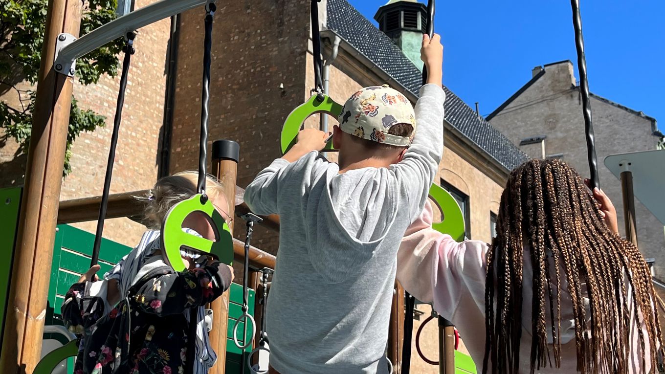 Tre barn som klatrer i klatrestativ i skolegården.