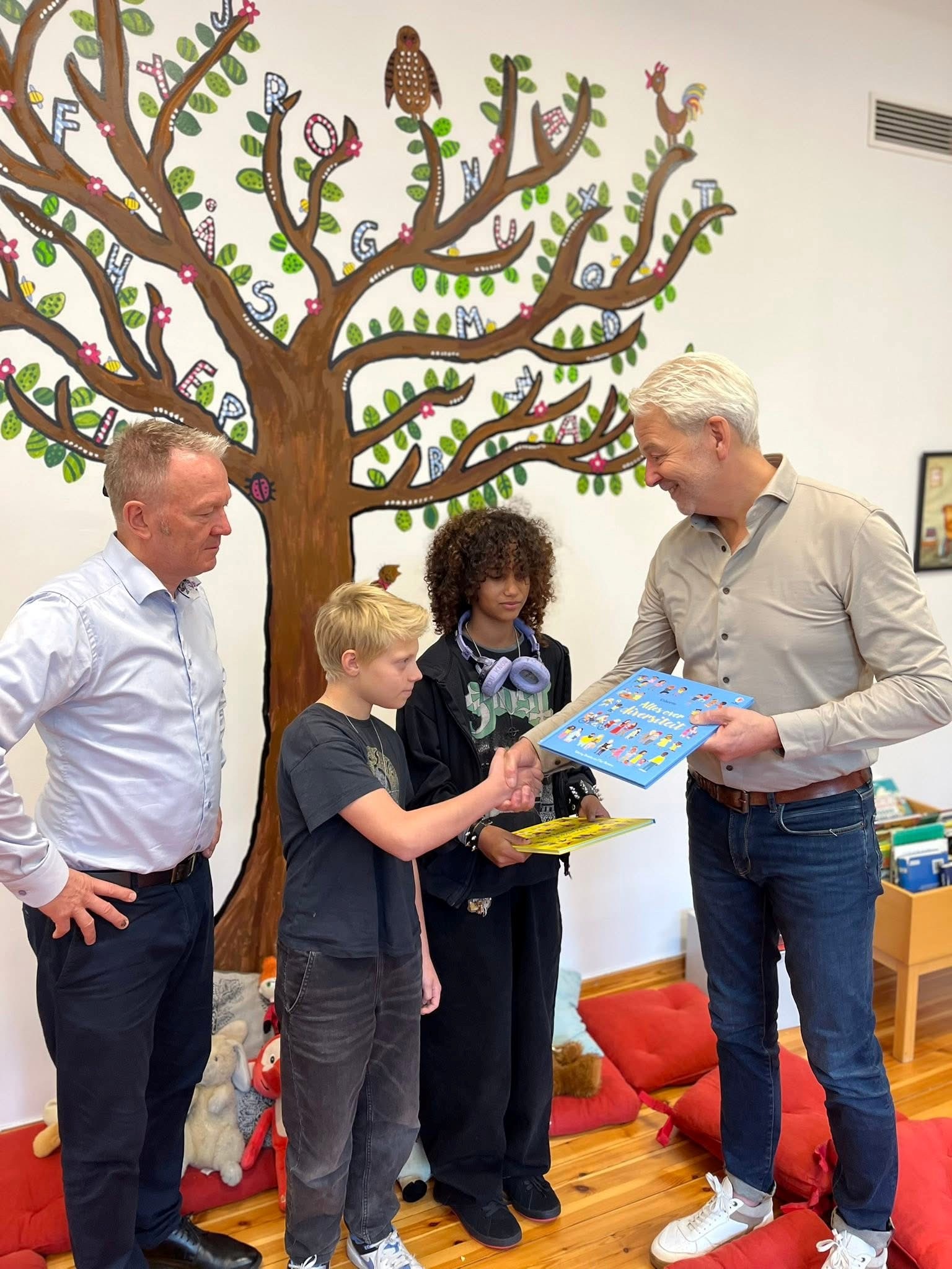 En gjest overrekker ei bok til to elever fra elevrådet