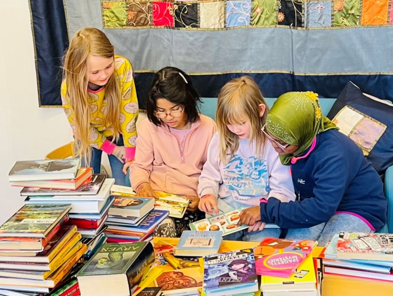 Elever i en sofa på biblioteket. En stabel med bøker på bordet.