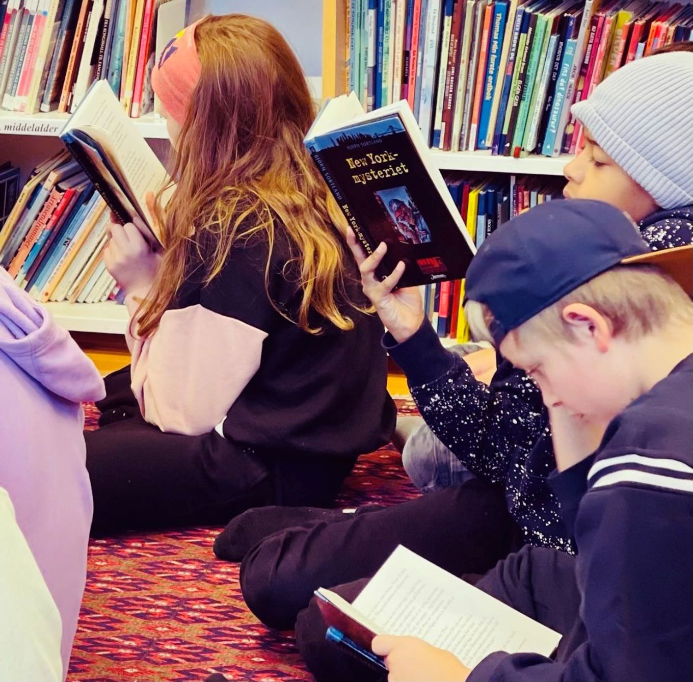 Elever sitter på et gulvteppe og leser.