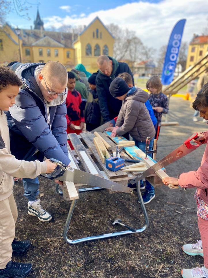 En gruppe personer som arbeider på et prosjekt utenfor skolen. Elevene sager og snekrer små biler.