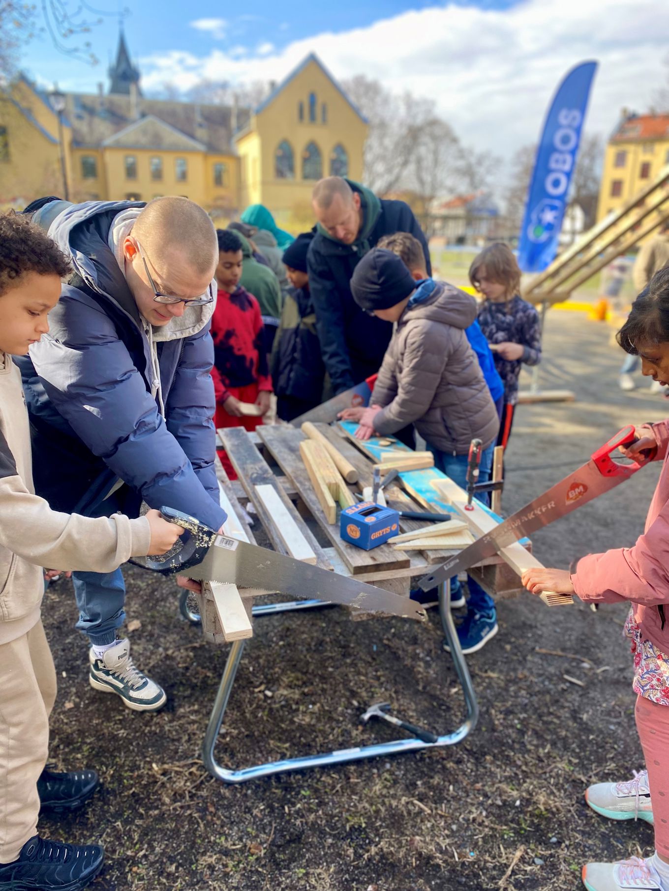 Foto: Charlotte Cappello Sylte En gruppe personer som arbeider på et prosjekt utenfor skolen. Elevene sager og snekrer små biler.