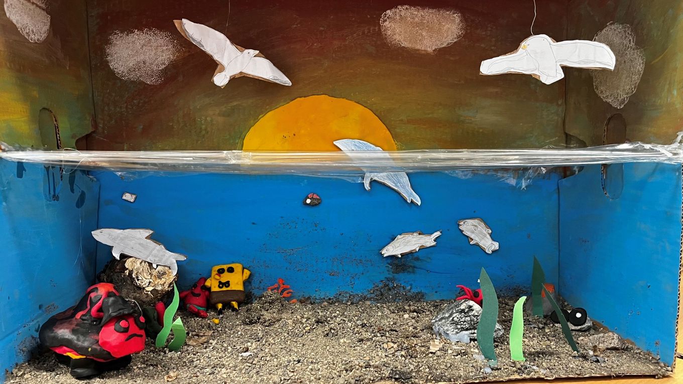 Et diorama lagd i en pappeske. Dioramaet viser livet over og under vann med fugler, sjøpattedyr og fisk.