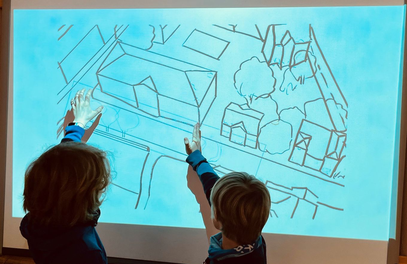 Elever står foran ei tavle og ser på ei skisse over skoleområdet. De  peker på bildet.