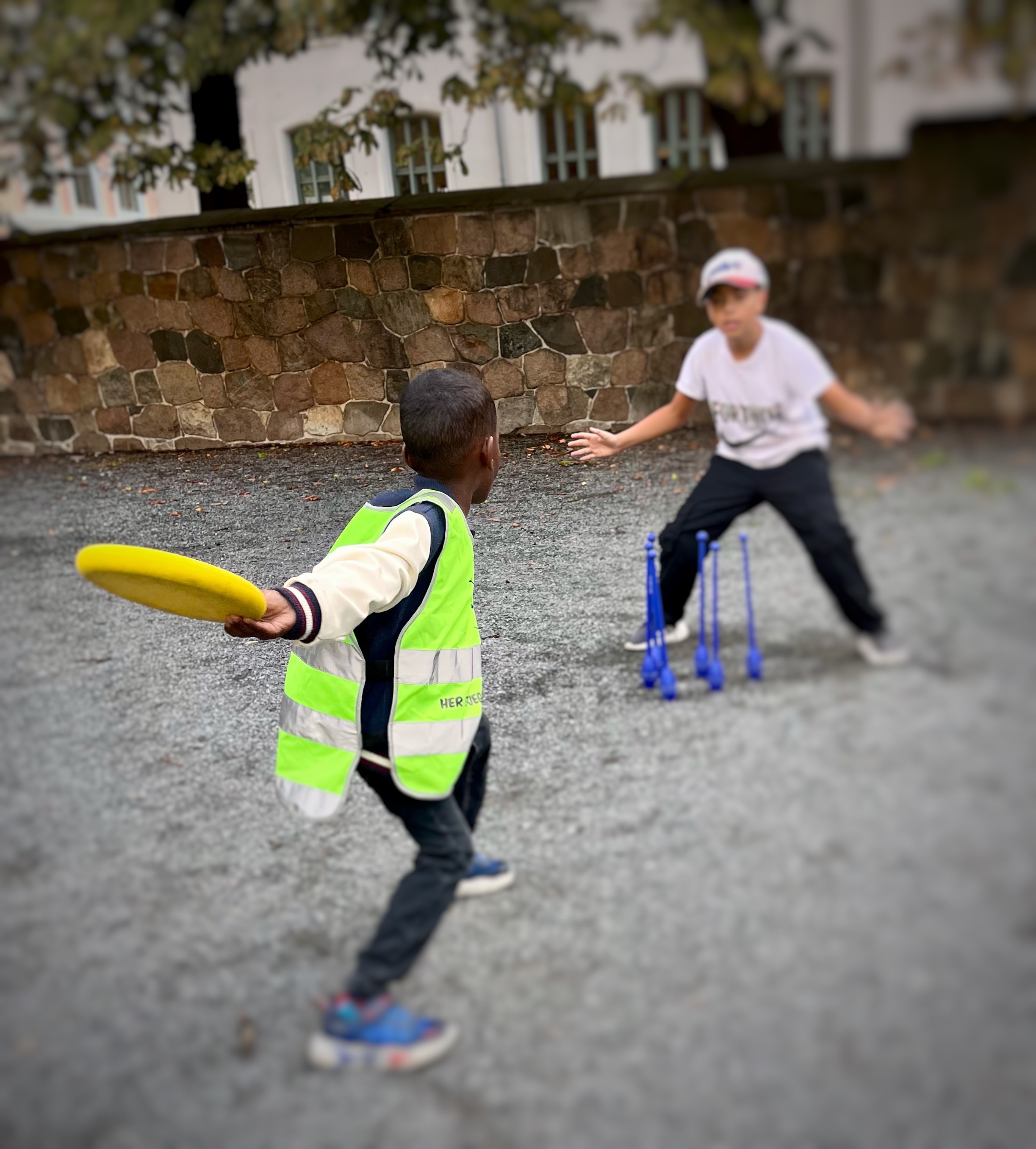 Tor barn som leker med en frisbee. Det ene barnet kaster frisbeen mot noen kjegler.