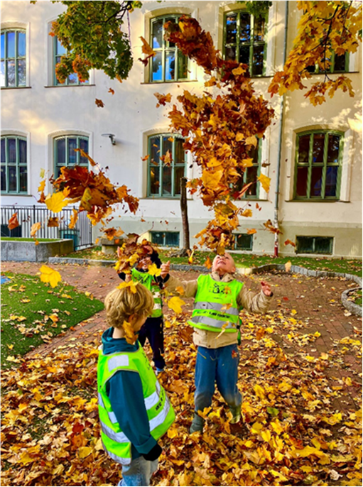 Et par barn som leker i en skolegård med løv på bakken.