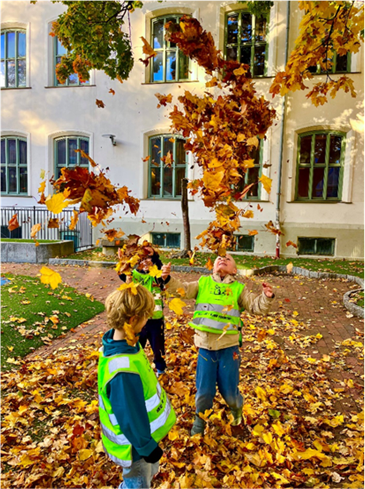 Et par barn som leker i en skolegård med løv på bakken.