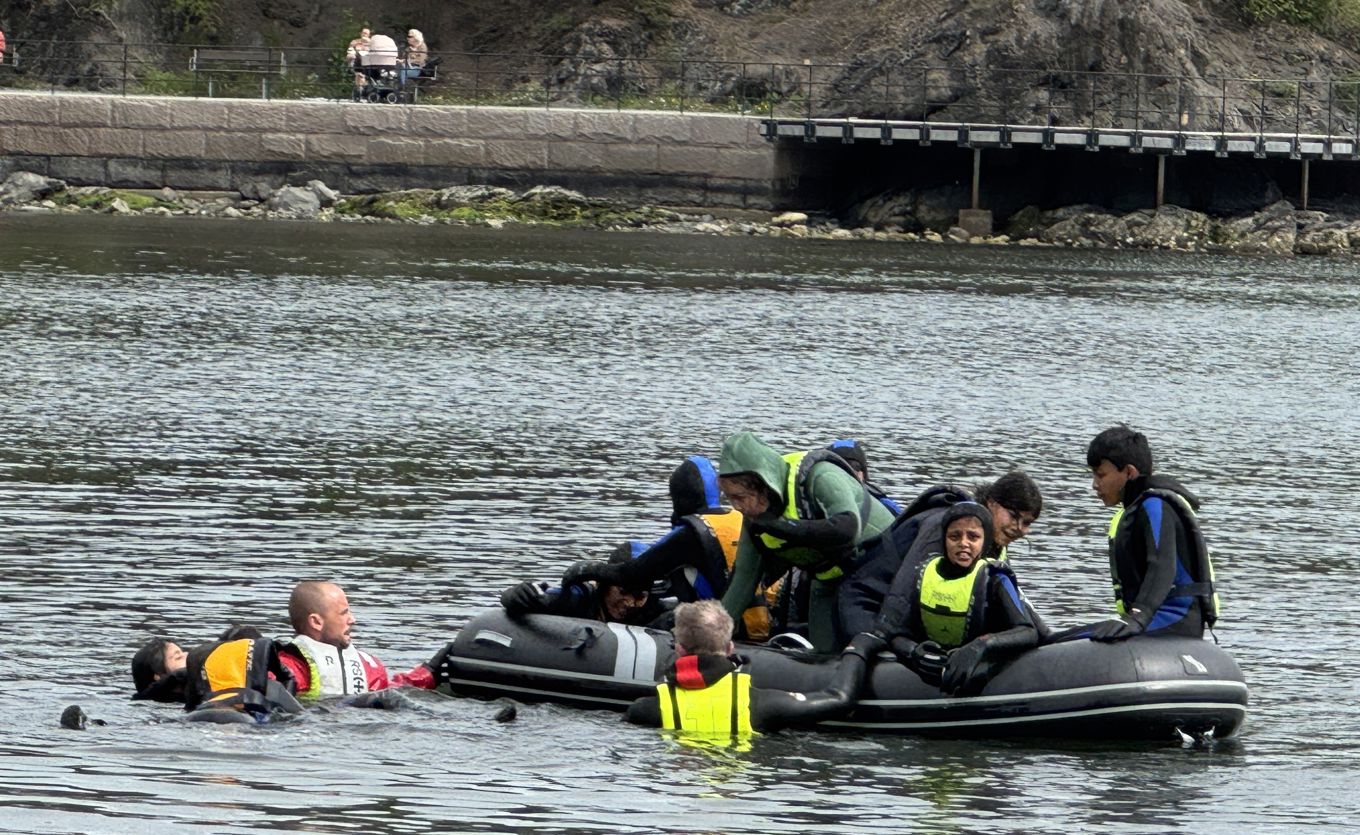 Elever øver på livredning. Noen sitter i en liten båt, mens andre flyter i vannet.