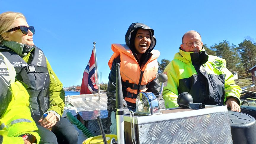 En elev står til rors i en åpen motorbåt. Hun smiler og ler.
