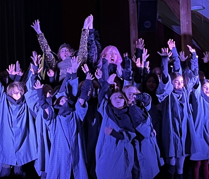 Elever og sangere står med hendene i været og synger opera.