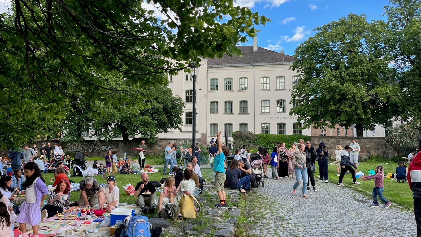 Piknik i parken ved Gamlebyen skole. Barn og voksne i parken. Skolebygget i bakgrunnen.