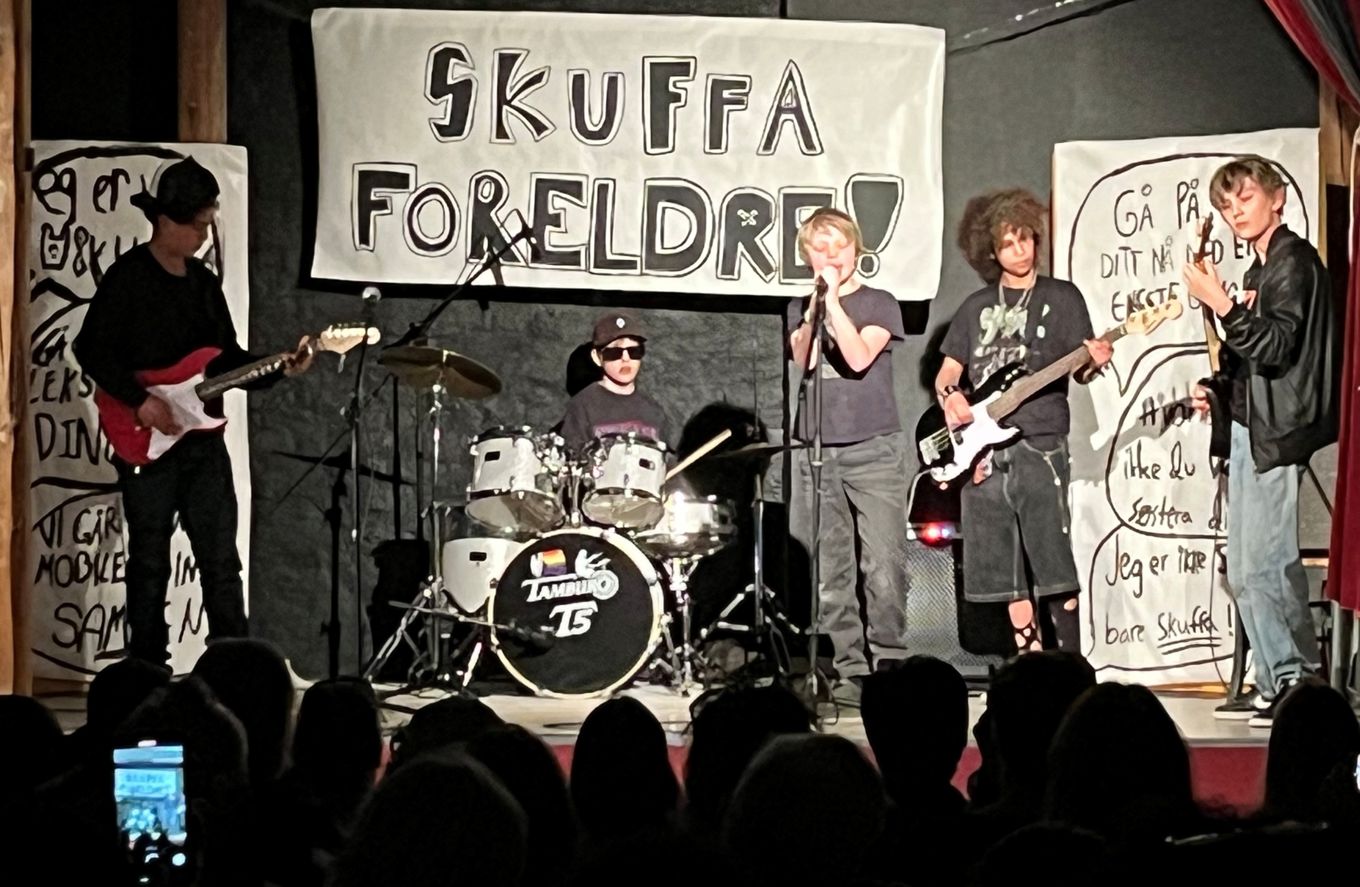 Et band med fem elever står på scenen og spiller rockekonsert. Et banner med tittel på konserten henger i bakgrunnen: Skuffa foreldre!