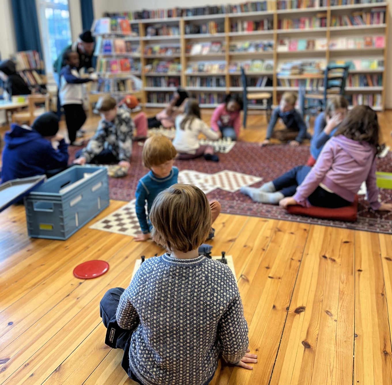 barn som sitter på gulvet i et bibliotek og spiller sjakk