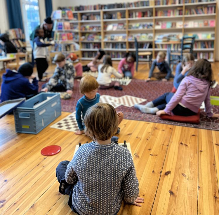 barn som sitter på gulvet i et bibliotek og spiller sjakk