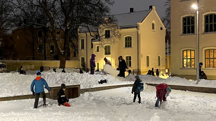 Barn som leker i snøen i skolegården. Det er tidlig morgen og fortsatt mørkt.